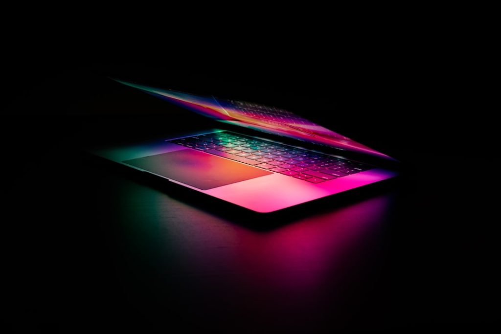 An illuminated laptop on a dark surface with colorful light reflections